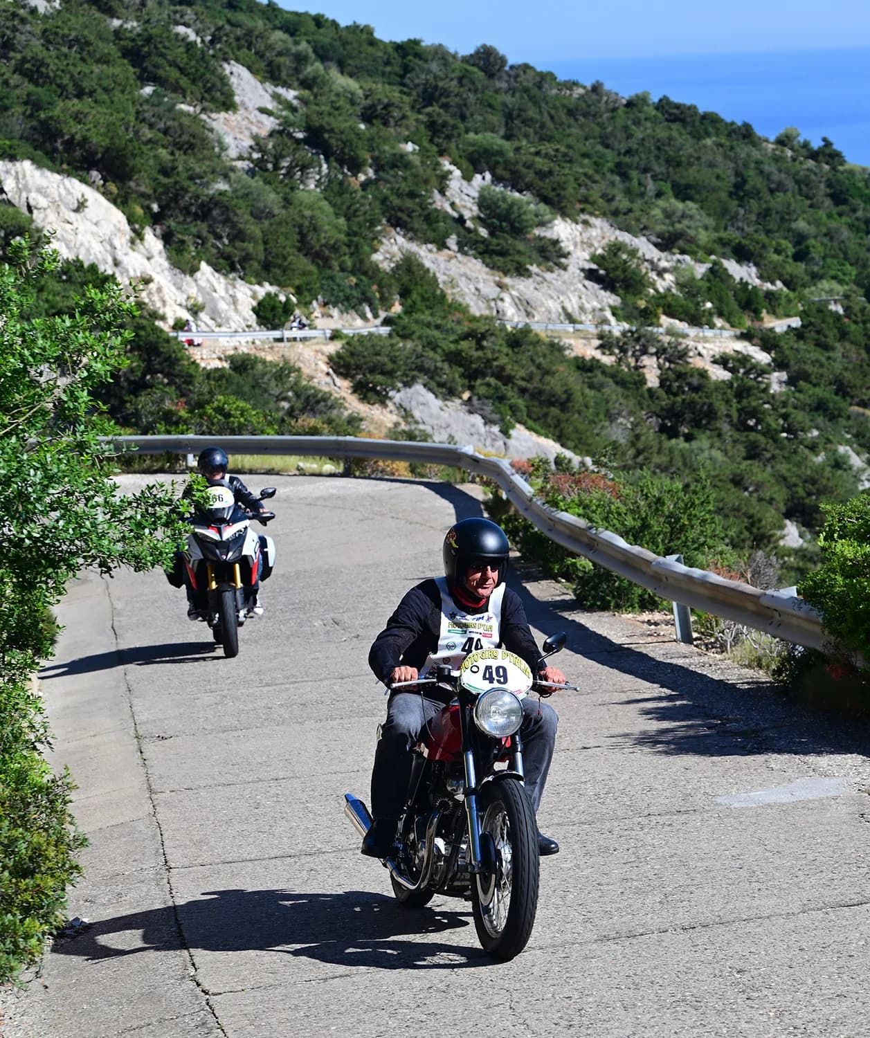 Moto storica in piega su strada panoramica con vista sul mare