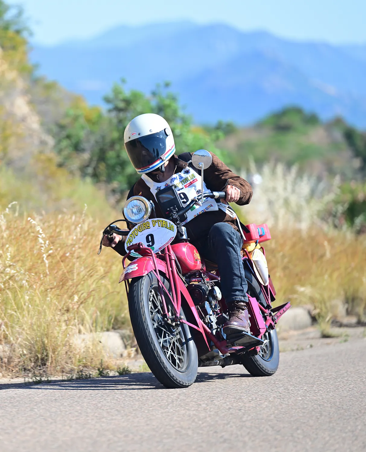 Moto storica in curva con vegetazione mediterranea